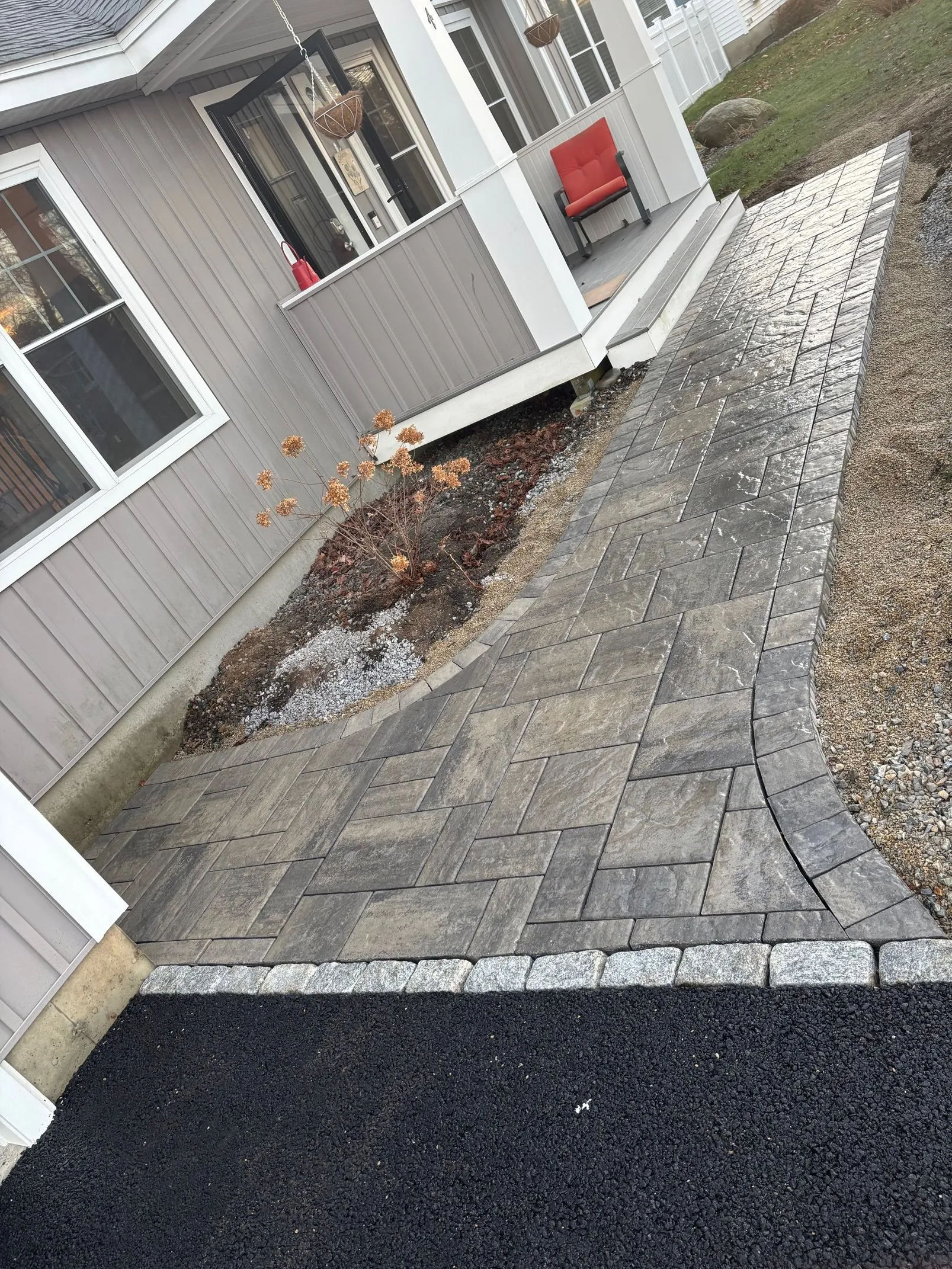 Paver walkway beside a home porch, finished with a granite cobble edge